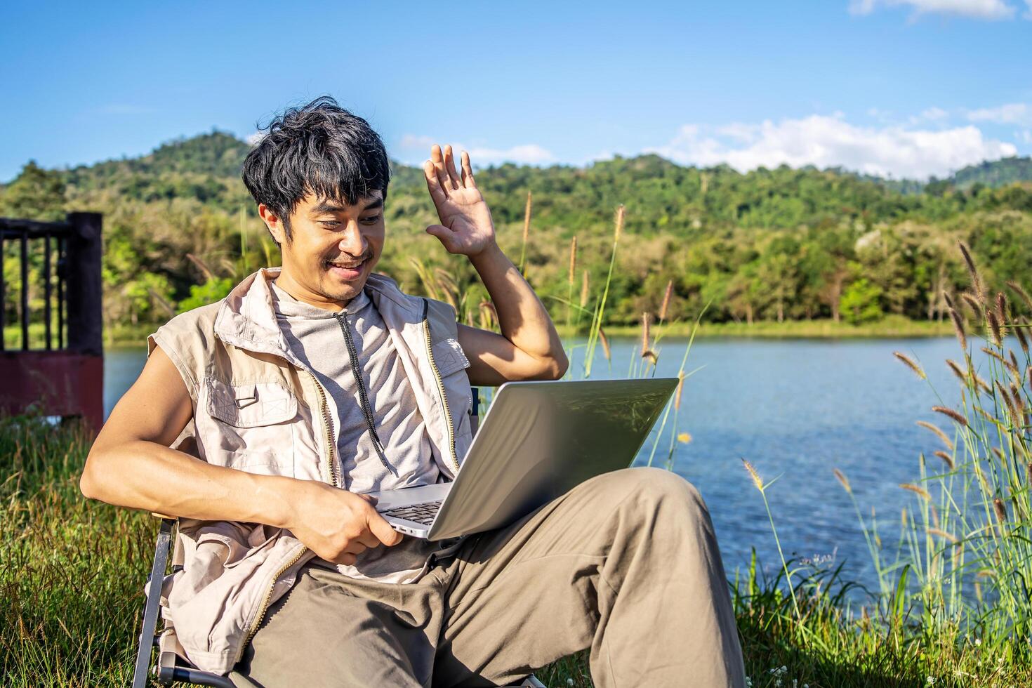 Young travel man relax and enjoy talking calling on on laptop, using laptop computer work remotely anywhere using internet connected to portable solar panel charging photo