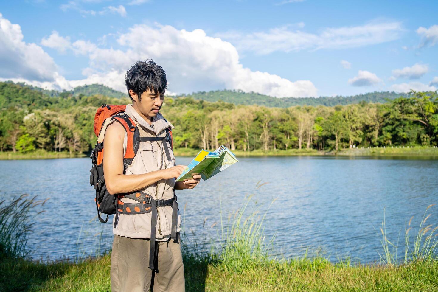 Young asian attractive male tourists looking for map in forest, Lost hiker male with backpacks reading travel map, Navigating and looking for directions in pine forest. Trekking concept. photo