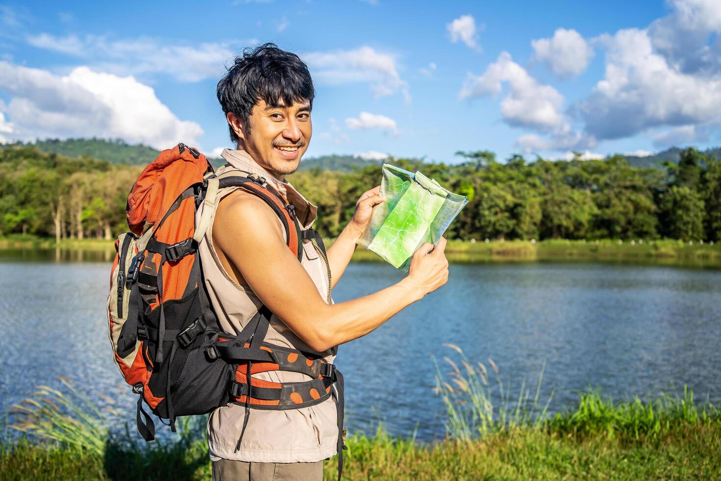 Young asian attractive male tourists looking for map in forest, Lost hiker male with backpacks reading travel map, Navigating and looking for directions in pine forest. Trekking concept. photo