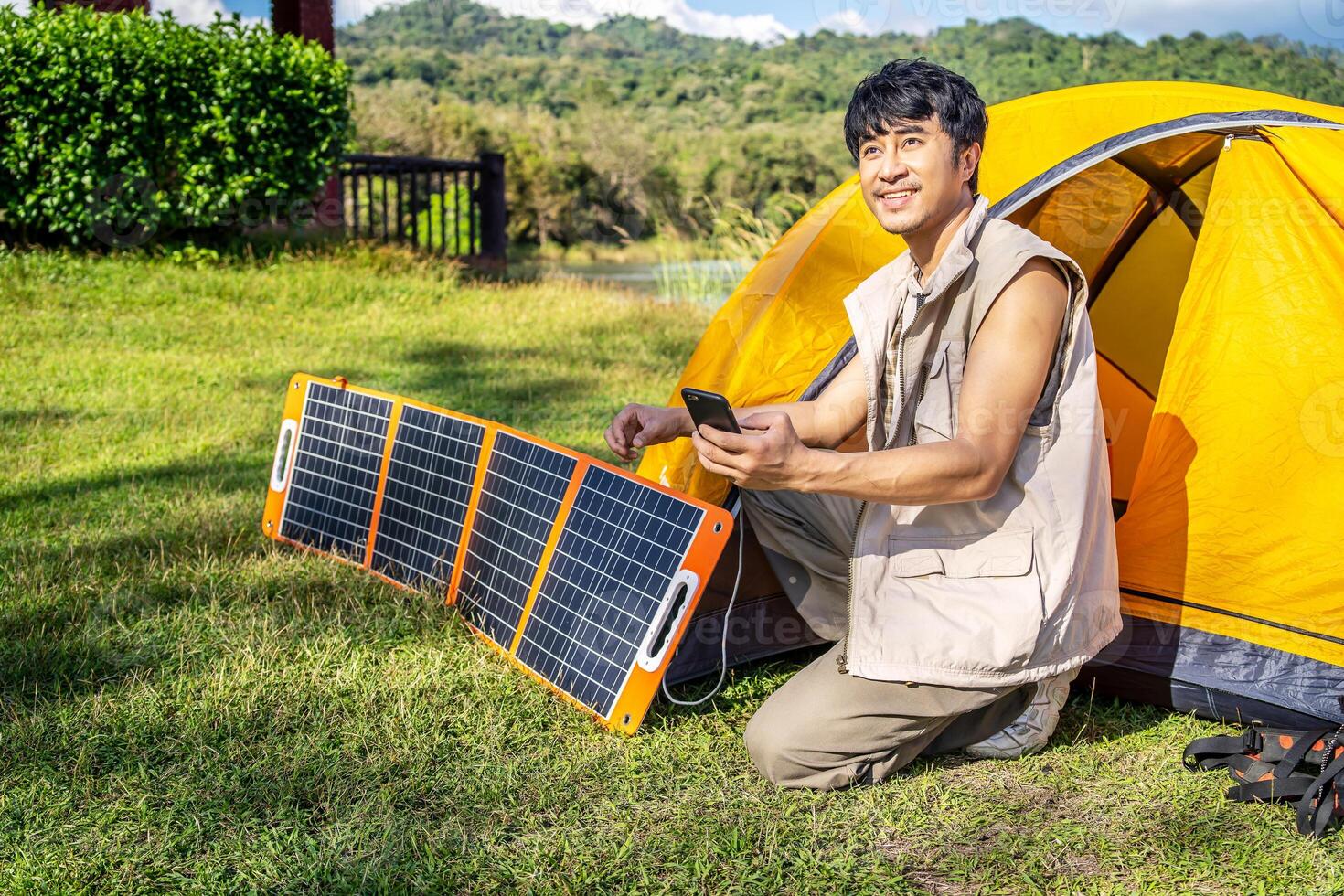 Young travel man relax and enjoy camping . Hand male plug in portable solar panel charging smartphone by multipurpose cable, Clean energy for using in camping or at home when no electricity photo
