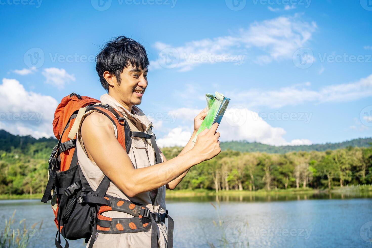 Young asian attractive male tourists looking for map in forest, Lost hiker male with backpacks reading travel map, Navigating and looking for directions in pine forest. Trekking concept. photo