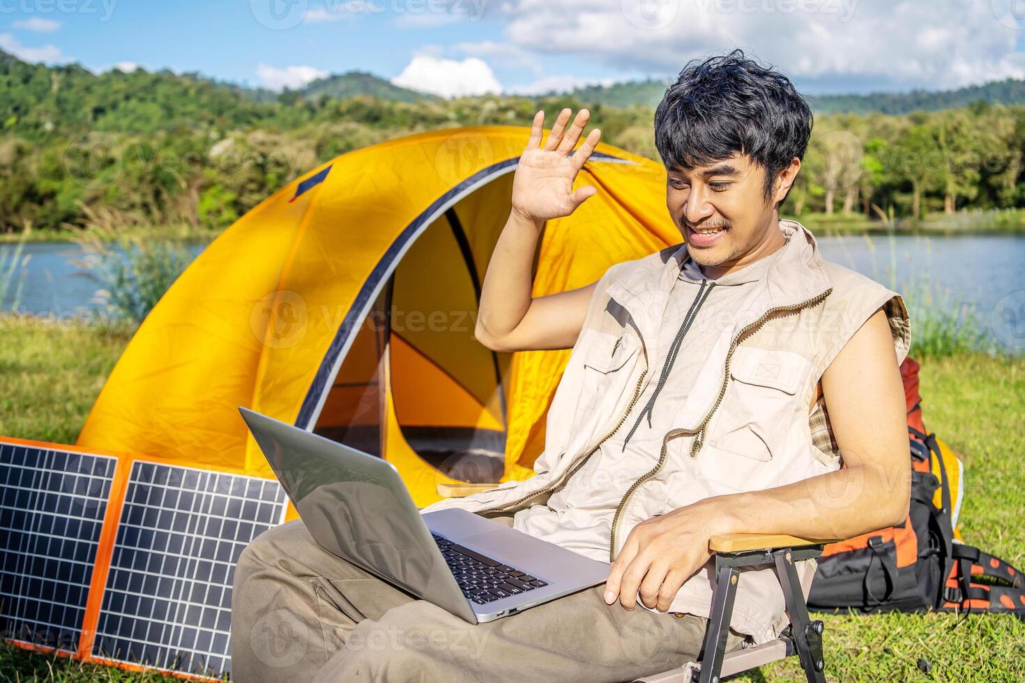 Young travel man relax and enjoy talking calling on on laptop, using laptop computer work remotely anywhere using internet connected to portable solar panel charging photo