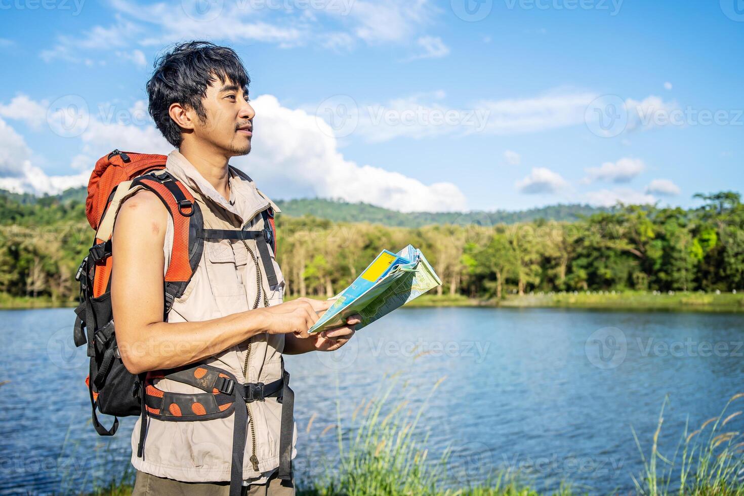 Young asian attractive male tourists looking for map in forest, Lost hiker male with backpacks reading travel map, Navigating and looking for directions in pine forest. Trekking concept. photo