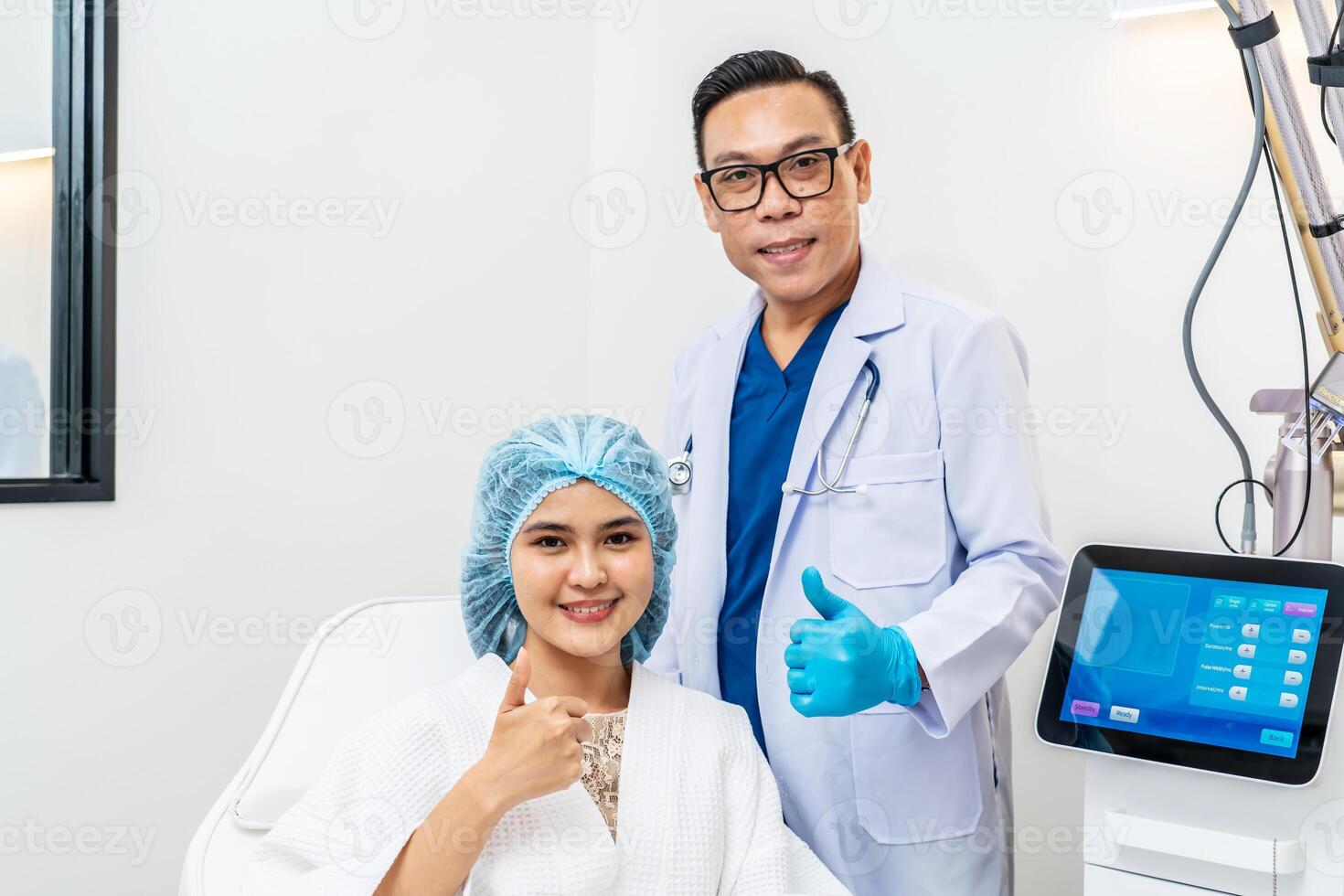 Front view of asian male cosmetologist and young woman patient with blue cap on head sitting in chair in cosmetological clinic , smiling, looking at camera, Concept of cosmetology. photo
