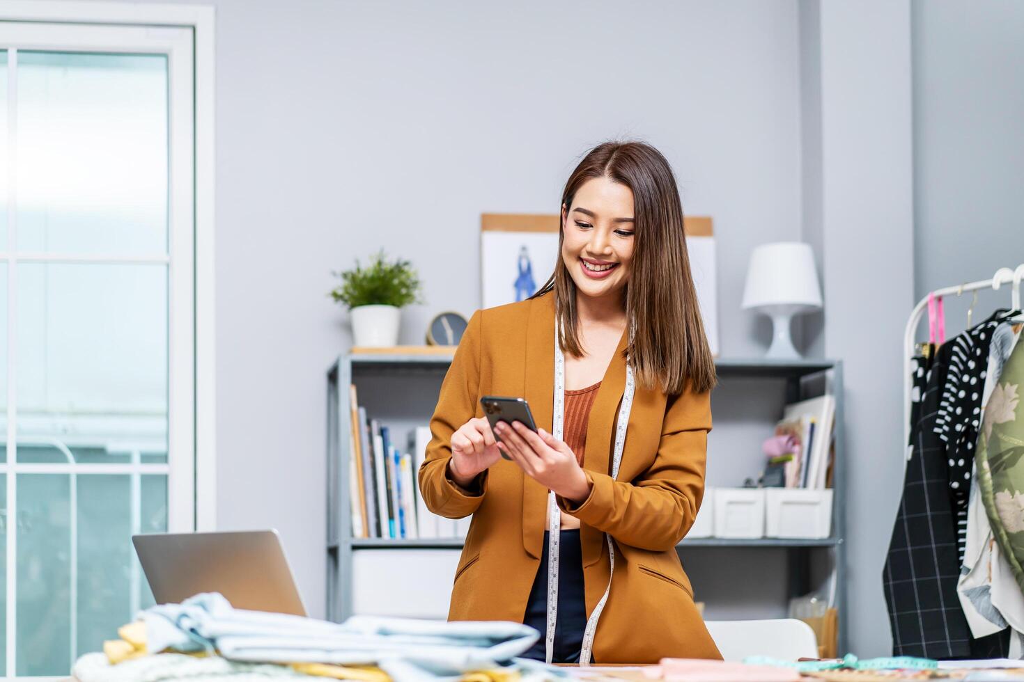 Negotiations online. Interested young woman cloths designer using cellphone at workplace in home office studio. Tailor dressmaker calling contacting client customer supplier to discuss order details photo
