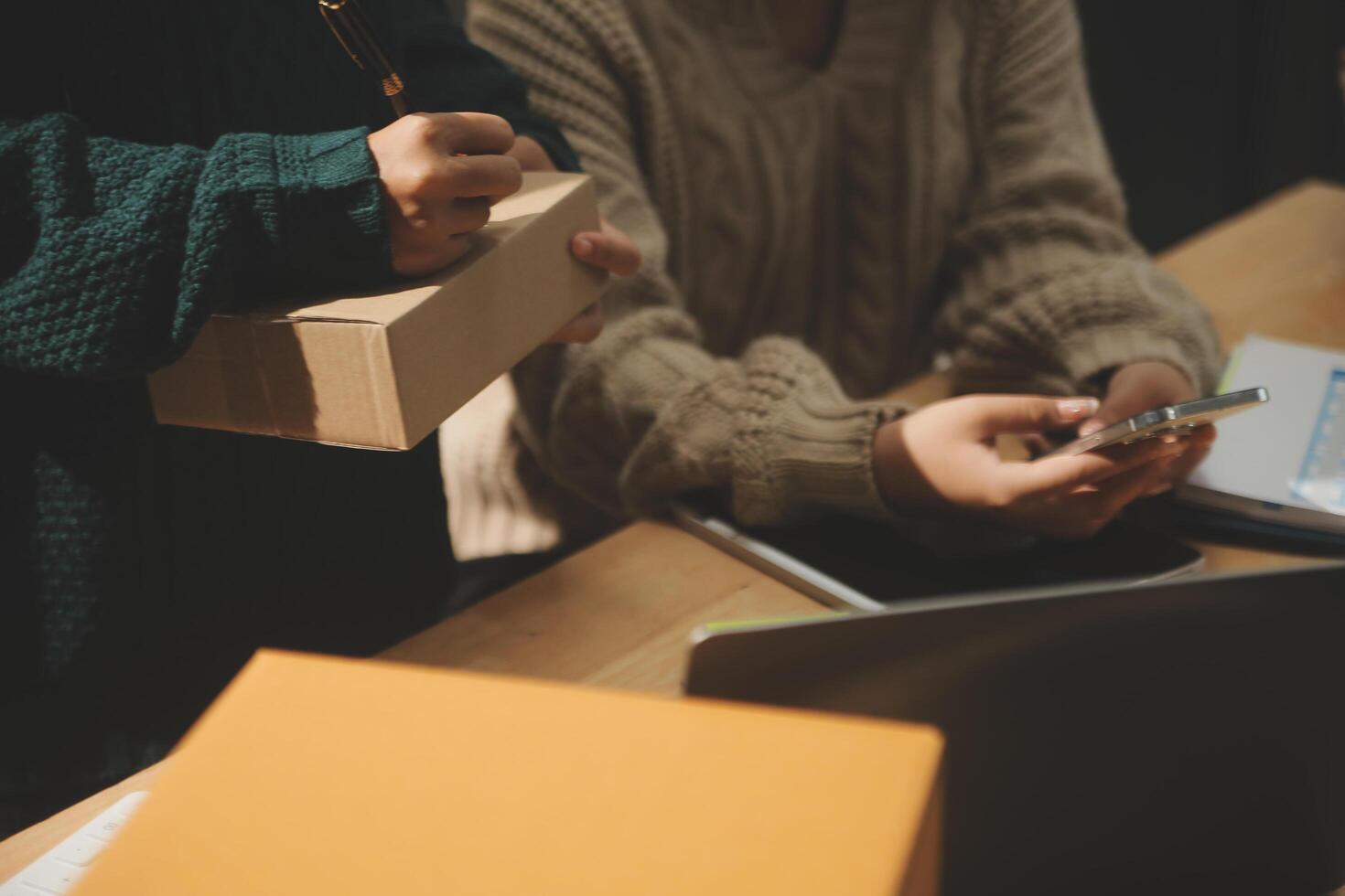 Startup small business SME, Entrepreneur owner African woman using smartphone or tablet taking receive and checking online purchase shopping order to preparing pack product box. photo