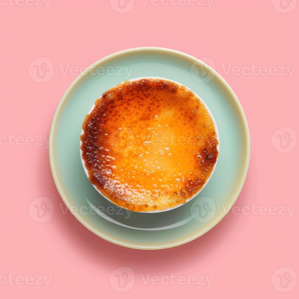 Overhead view of a delicious creme brulee dessert with a crispy caramelized sugar crust, served in a white ramekin on a blue saucer on a pink background photo