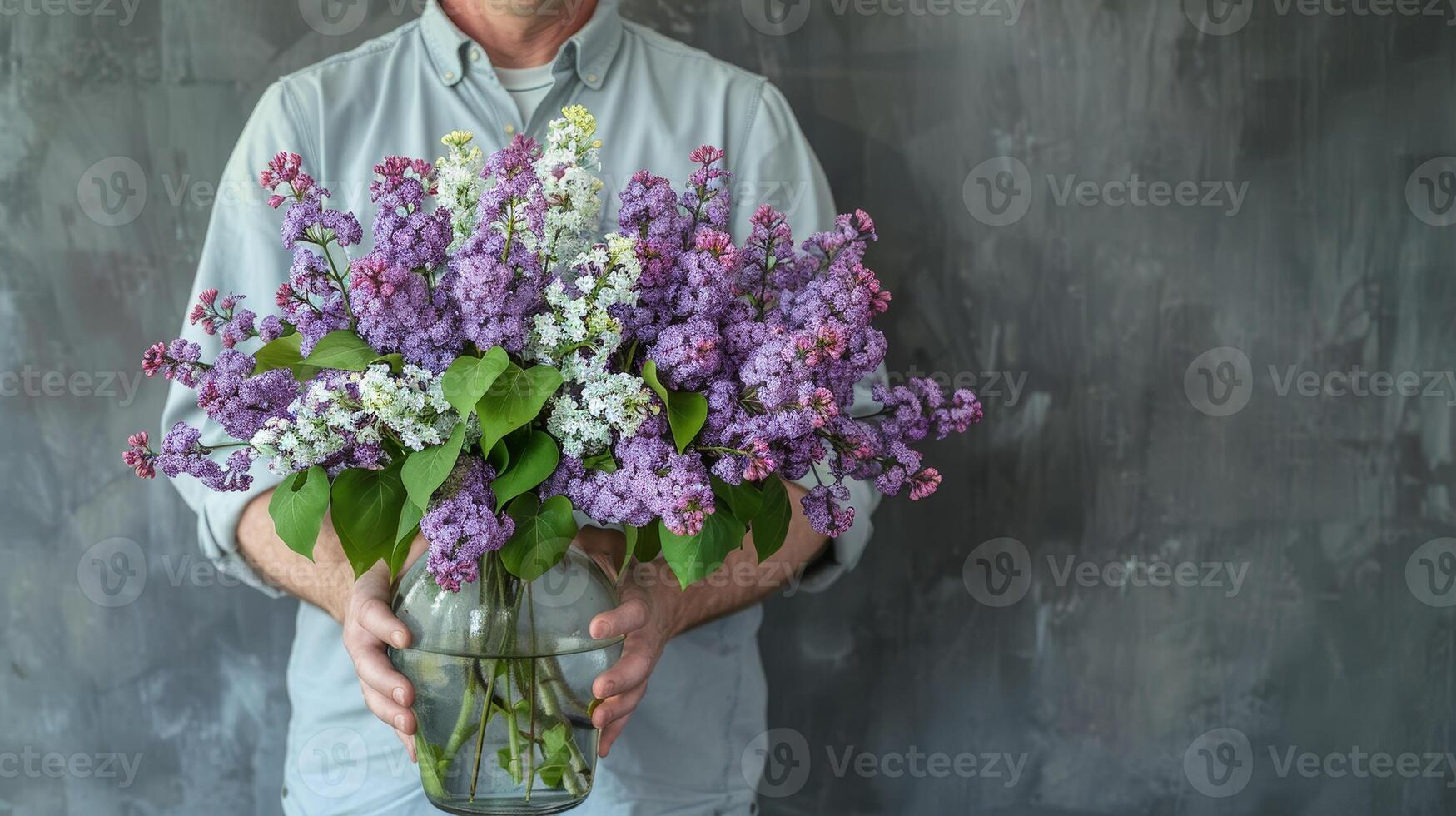 Elegant Man Holding a Beautiful Vase of Purple and White Lilacs in Studio Light against Slate Grey Background photo