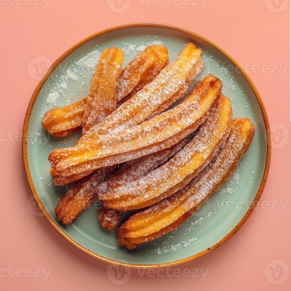 Close up view of fresh churros dusted with powdered sugar on a teal plate. photo