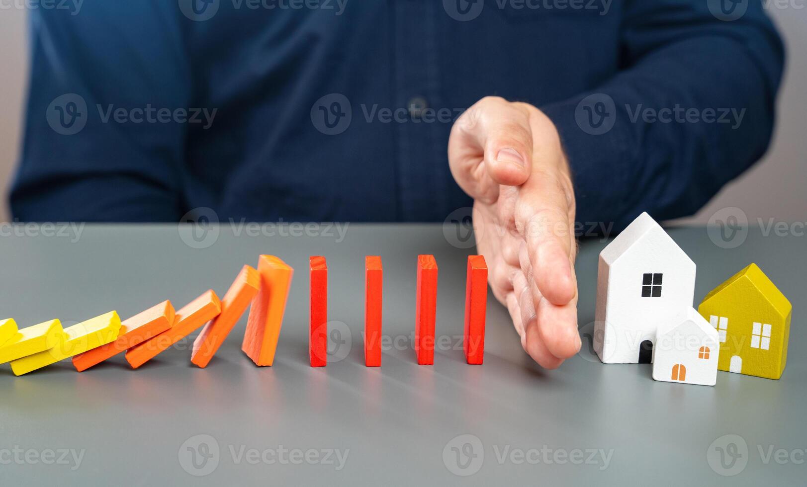 A man stops dominoes falling on a house with his hand. Protect property from threats and dangers. Real estate insurance, legal protection of property rights. photo