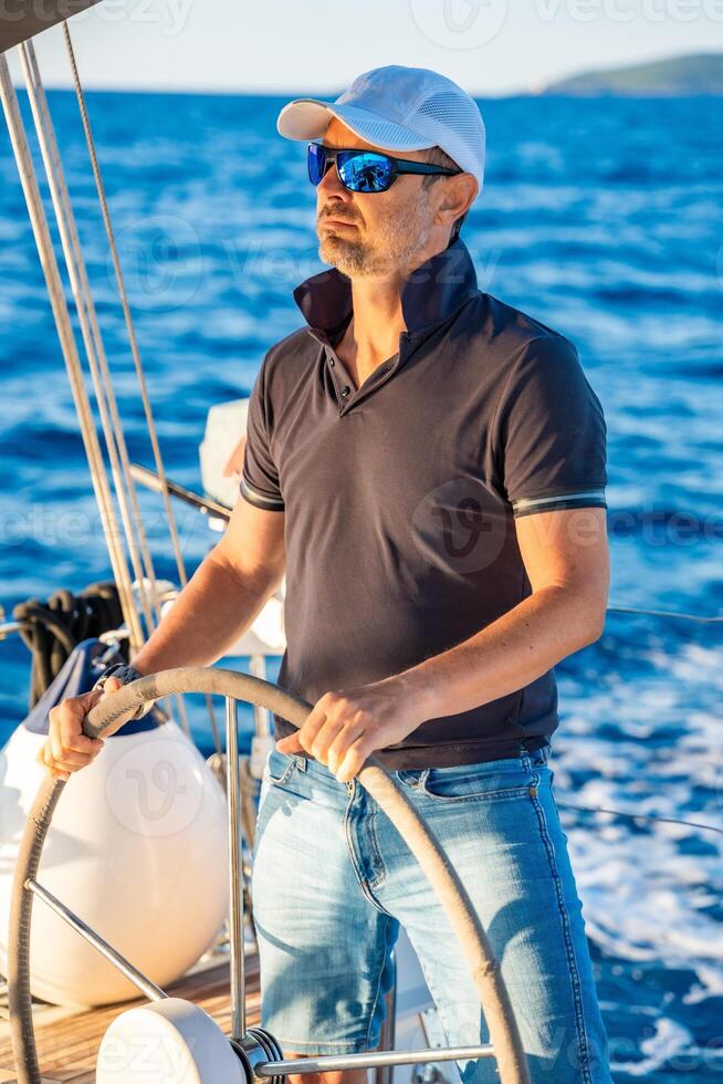 Young man captain stands at the helm and controls a sailboat during a journey by sea. High quality photo