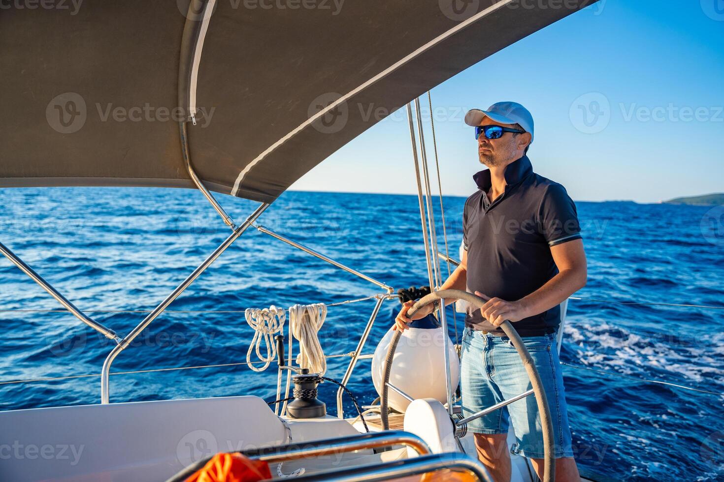 Young man captain stands at the helm and controls a sailboat during a journey by sea. High quality photo