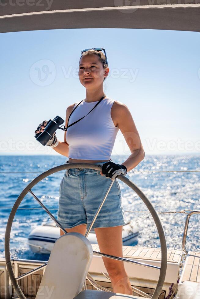 Young female captain on the yacht looking through binoculars during sailing boat control. Travel and active life. Yachting. High quality photo