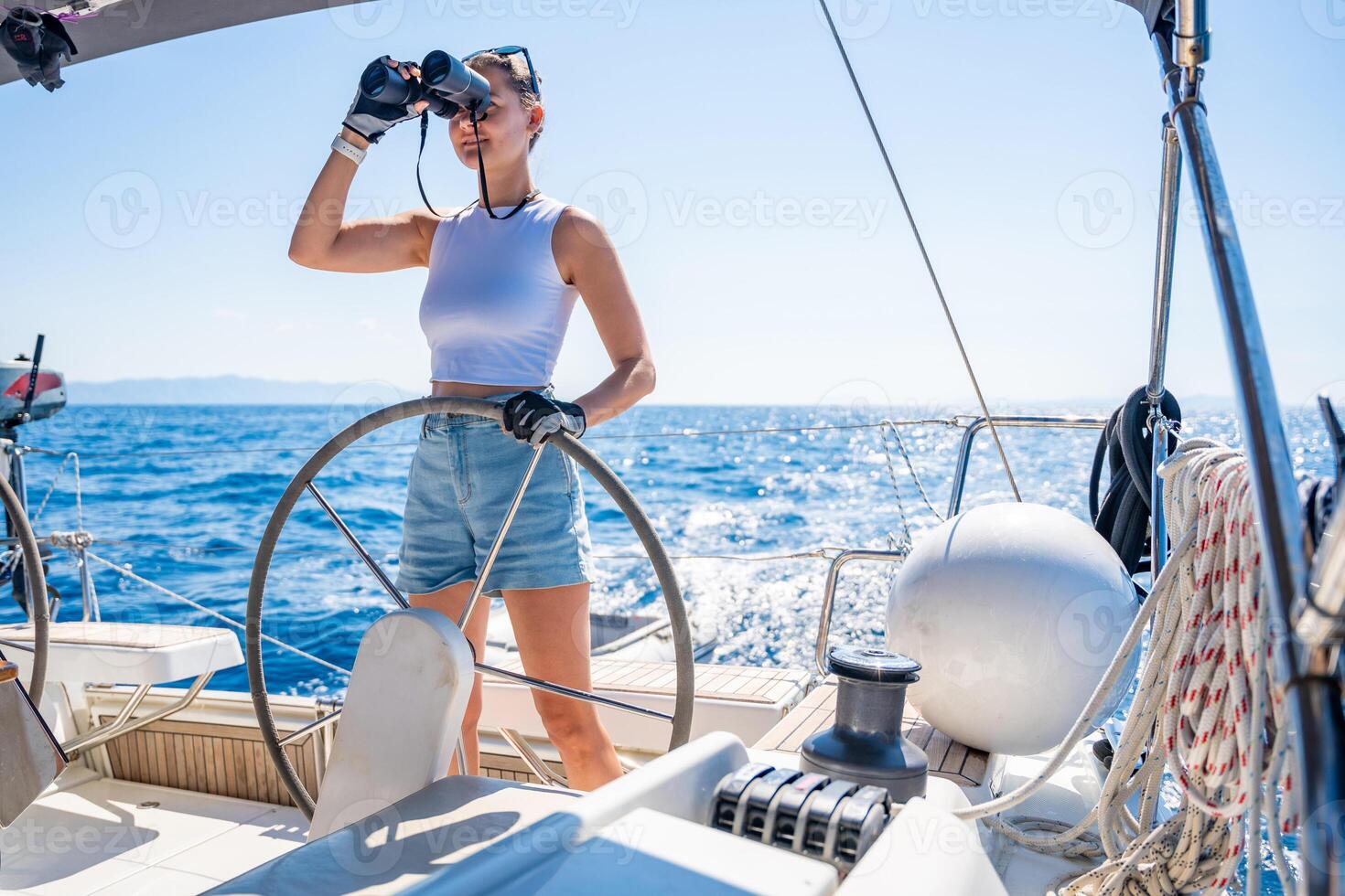 Young female captain on the yacht looking through binoculars during sailing boat control. Travel and active life. Yachting. High quality photo
