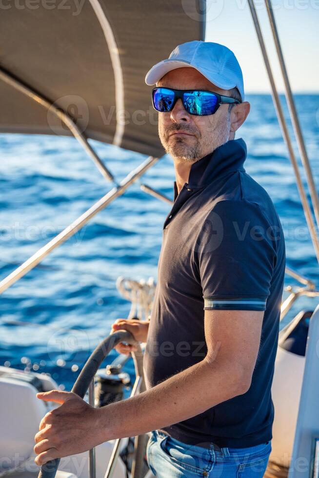 Young man captain stands at the helm and controls a sailboat during a journey by sea. High quality photo