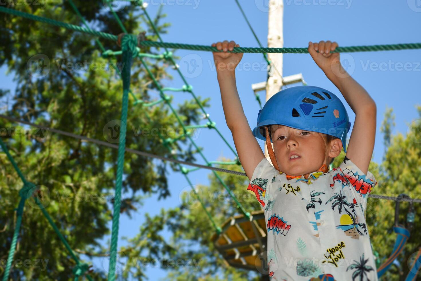 The child is a tightrope walker. Rope park. A boy teenager in a helmet walks on suspended rope ladders. Carabiners and safety straps. Safety. Summer activity. Sport. Children's playground in nature photo