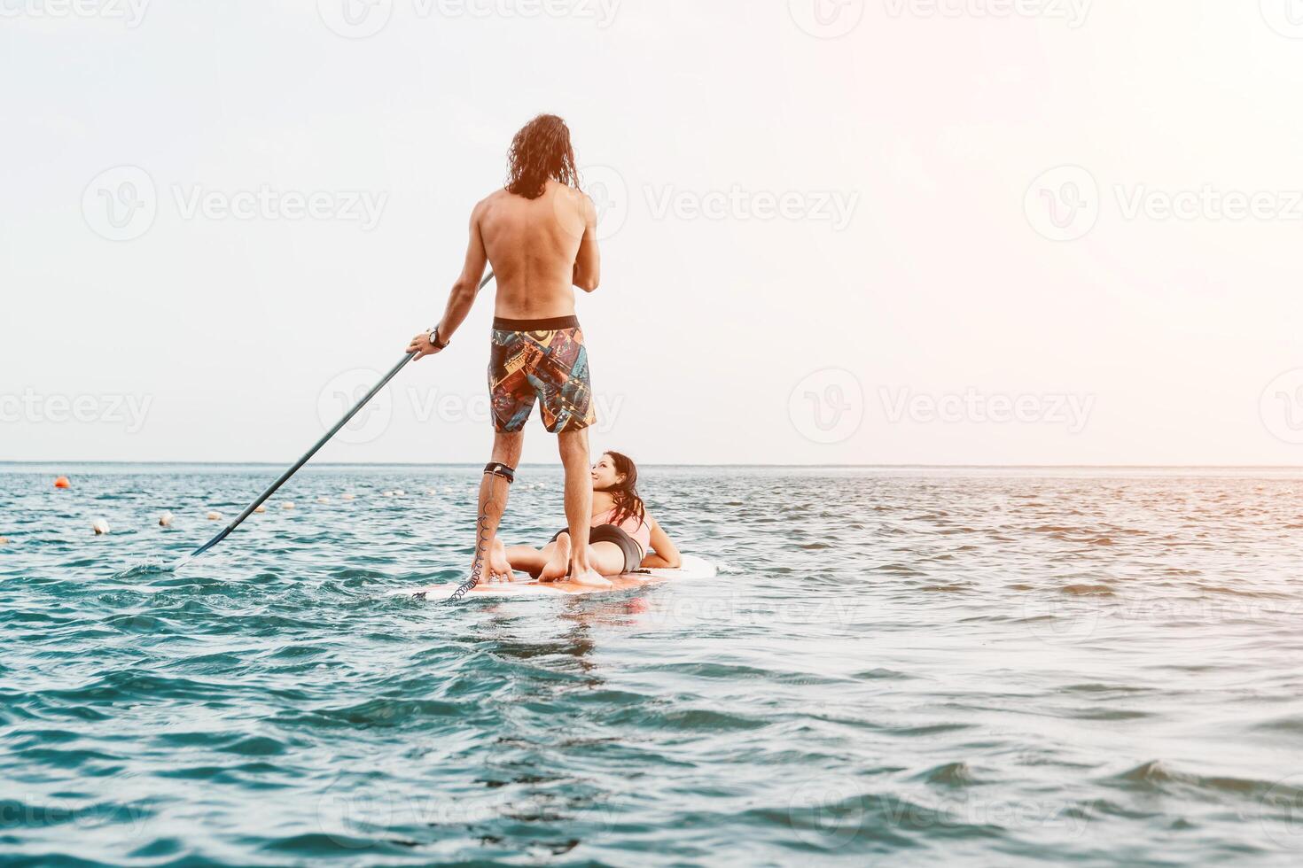 Sea woman and man on sup. Silhouette of happy young woman and man, surfing on SUP board, confident paddling through water surface. Idyllic sunset. Active lifestyle at sea or river. Slow motion photo