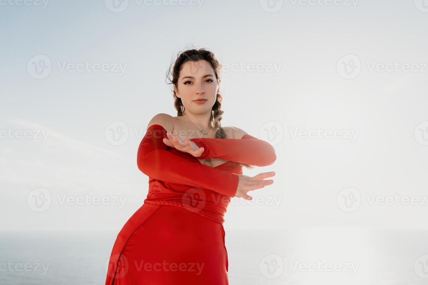 Closeup portrait of sensual young brunette woman in red dress, happily dancing outdoors isolated on blurry sea background with natural bokeh in soft warm sunset backlight. Selective focus. photo