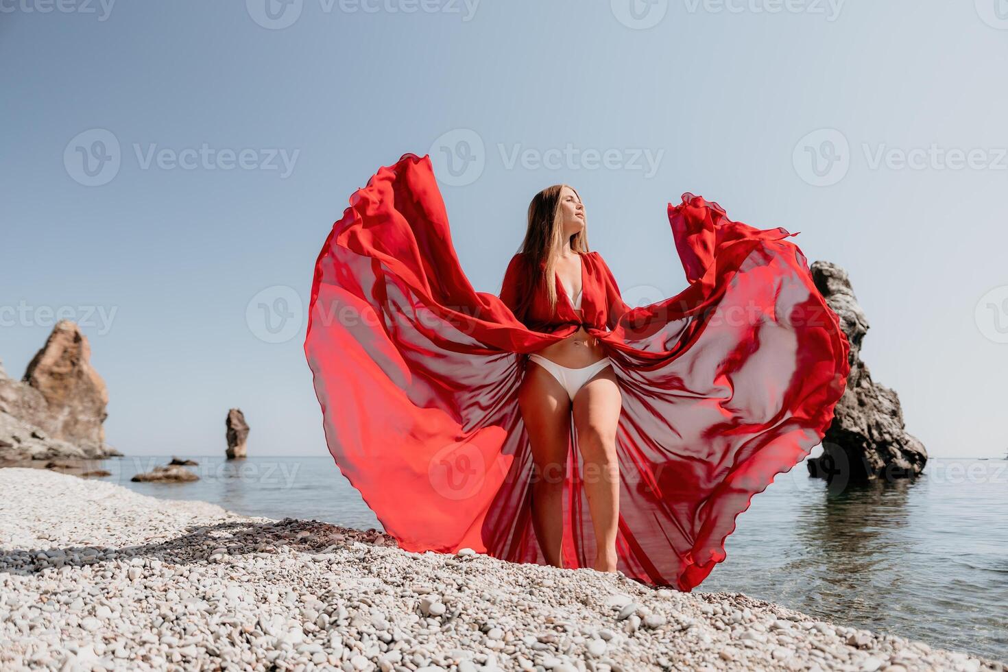 Woman travel sea. Happy tourist in red dress enjoy taking picture outdoors for memories. Woman traveler posing on the rock at sea bay surrounded by volcanic mountains, sharing travel adventure journey photo