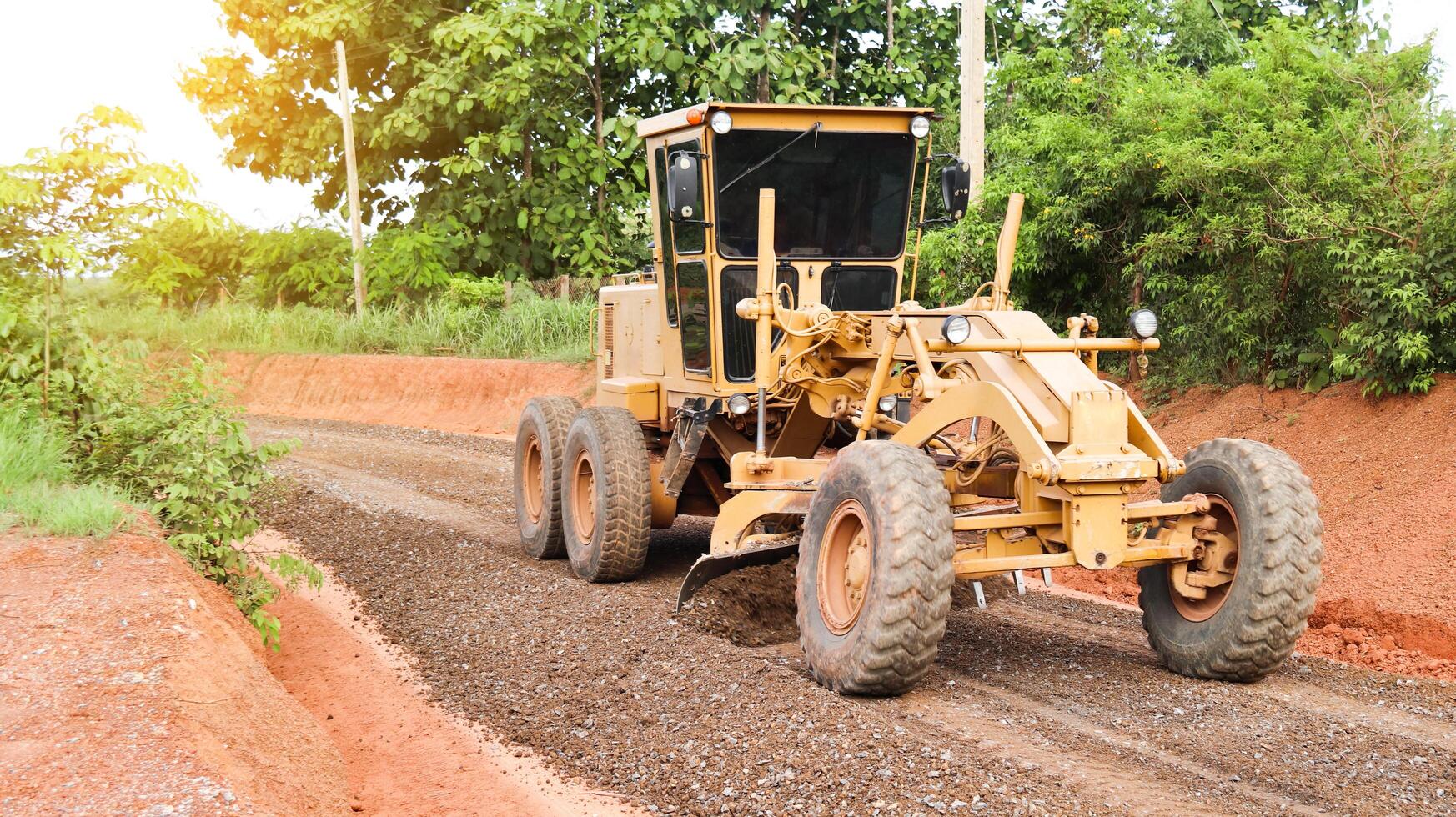 Image of a grader machine leveling gravels on a dirt road in preparation for asphalt paving for new road construction. photo