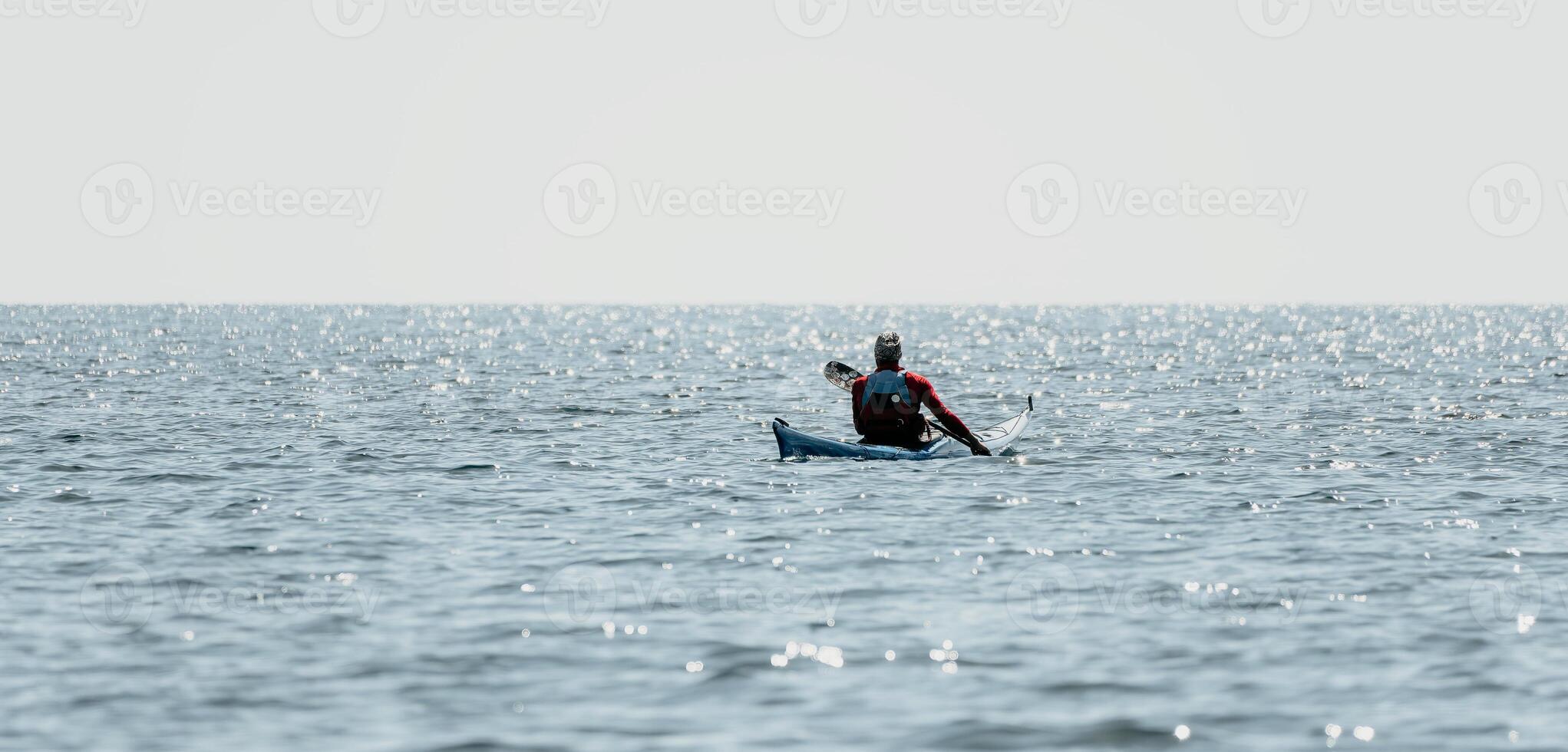 Man sea kayak. Happy free man in kayak on ocean, paddling with wooden oar. Calm sea water and horizon in background. Active lifestyle at sea. Summer vacation. photo