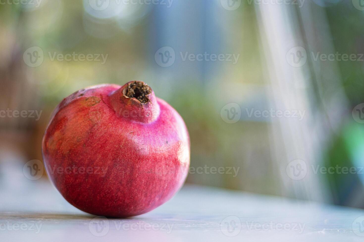 Vibrant whole fresh pomegranate captured in natural light. Ripe and juicy fruit isolated against a soft focus background. Perfect for healthy lifestyle content, culinary websites. Copy space. photo