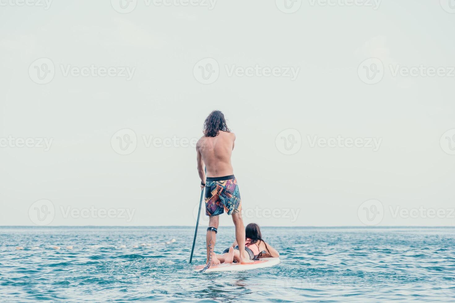 Sea woman and man on sup. Silhouette of happy young woman and man, surfing on SUP board, confident paddling through water surface. Idyllic sunset. Active lifestyle at sea or river. photo