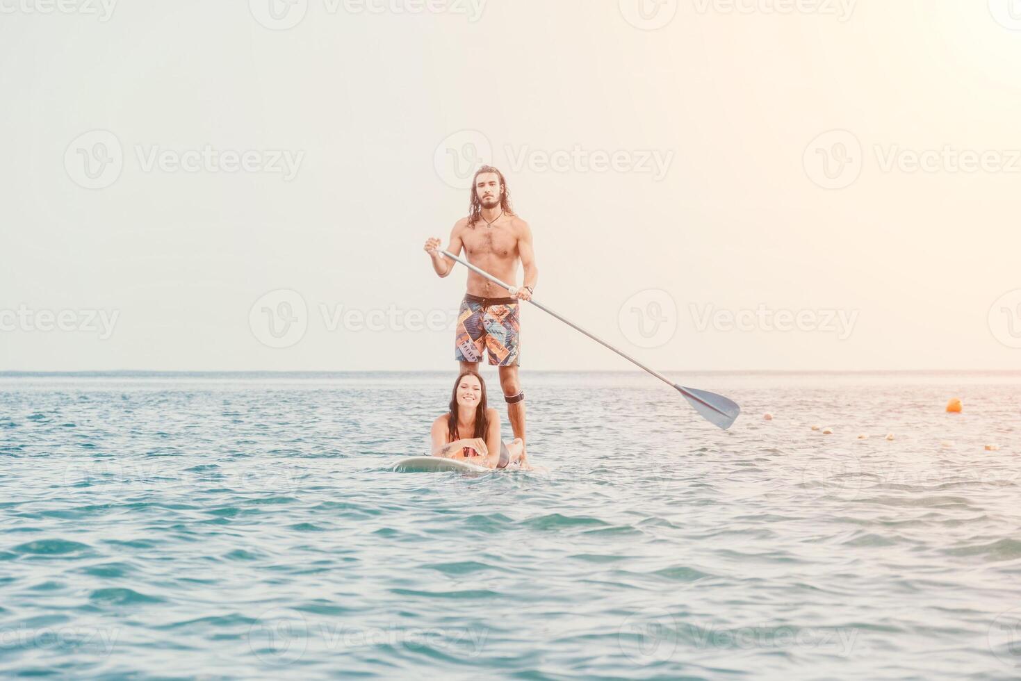 Sea woman and man on sup. Silhouette of happy young woman and man, surfing on SUP board, confident paddling through water surface. Idyllic sunset. Active lifestyle at sea or river. photo