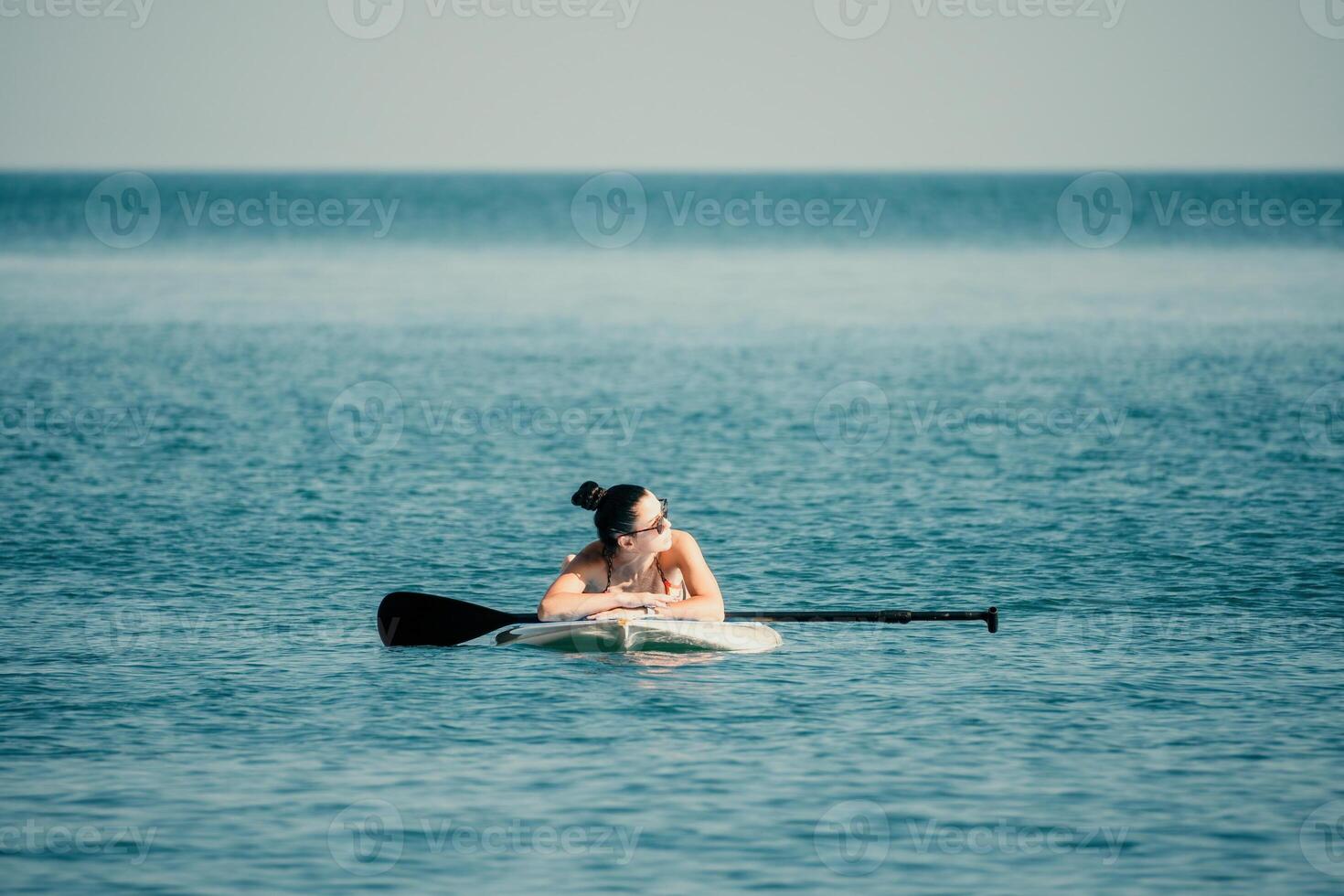 Sea woman sup. Silhouette of happy middle aged tanned woman in rainbow bikini, surfing on SUP board, confident paddling through water surface. Idyllic sunset. Active lifestyle at sea or river. photo