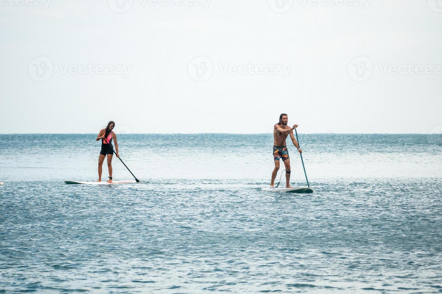 Sea woman and man on sup. Silhouette of happy young woman and man, surfing on SUP board, confident paddling through water surface. Idyllic sunset. Active lifestyle at sea or river. photo