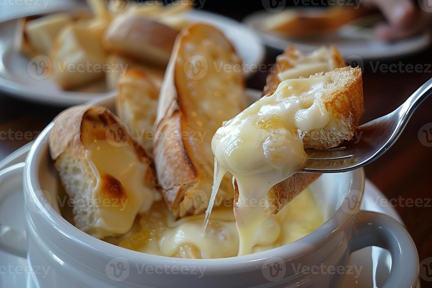 Fork dipping bread in melted cheese fondue with more bread in background photo