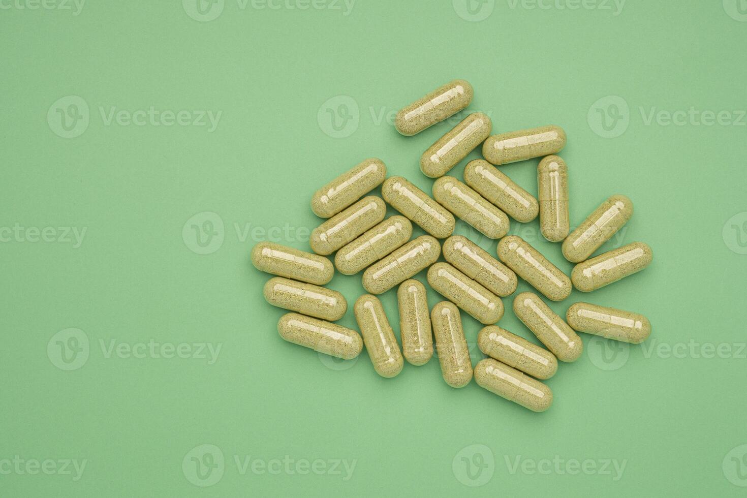 Flat lay of Andrographis paniculata capsules isolated on a green background. Space for text. Herbal, medicine, and healthcare concept photo