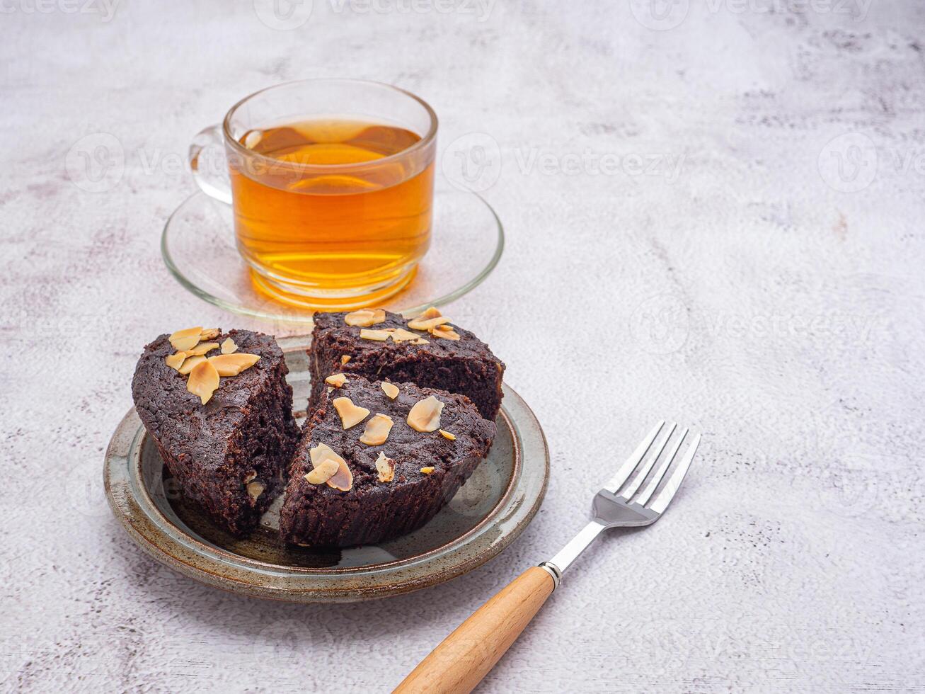 Pieces of fresh brownies on a plate with a teacup on cement background. Side view. Delicious chocolate pie. Dessert and relaxation concept photo