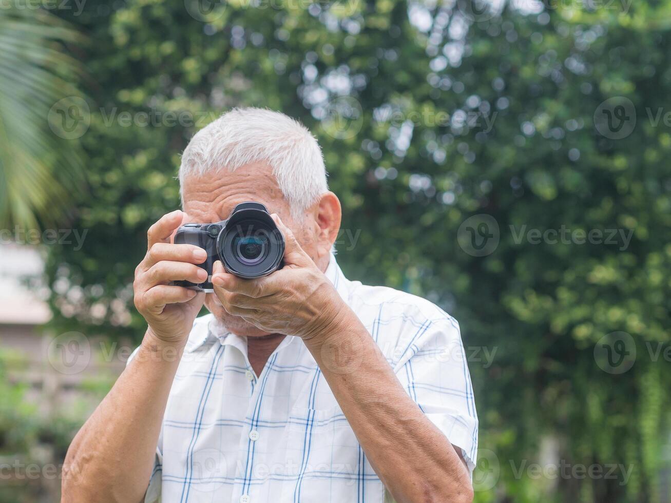 Happy senior man taking photographs with a digital camera while standing outdoors. Aged people photographer and relaxation concept photo