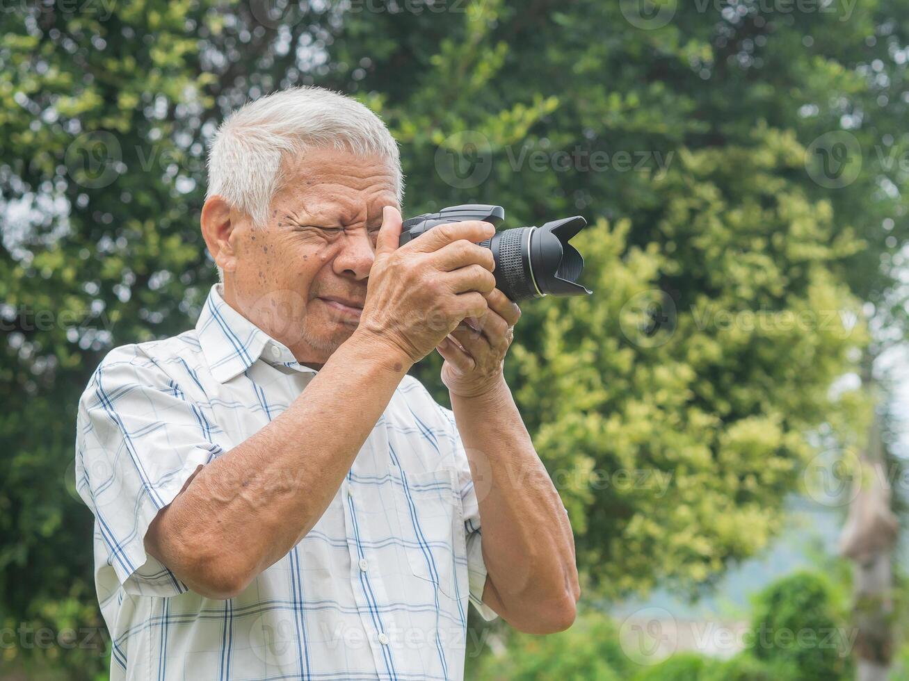 Happy senior man taking photographs with a digital camera while standing outdoors. Aged people photographer and relaxation concept photo