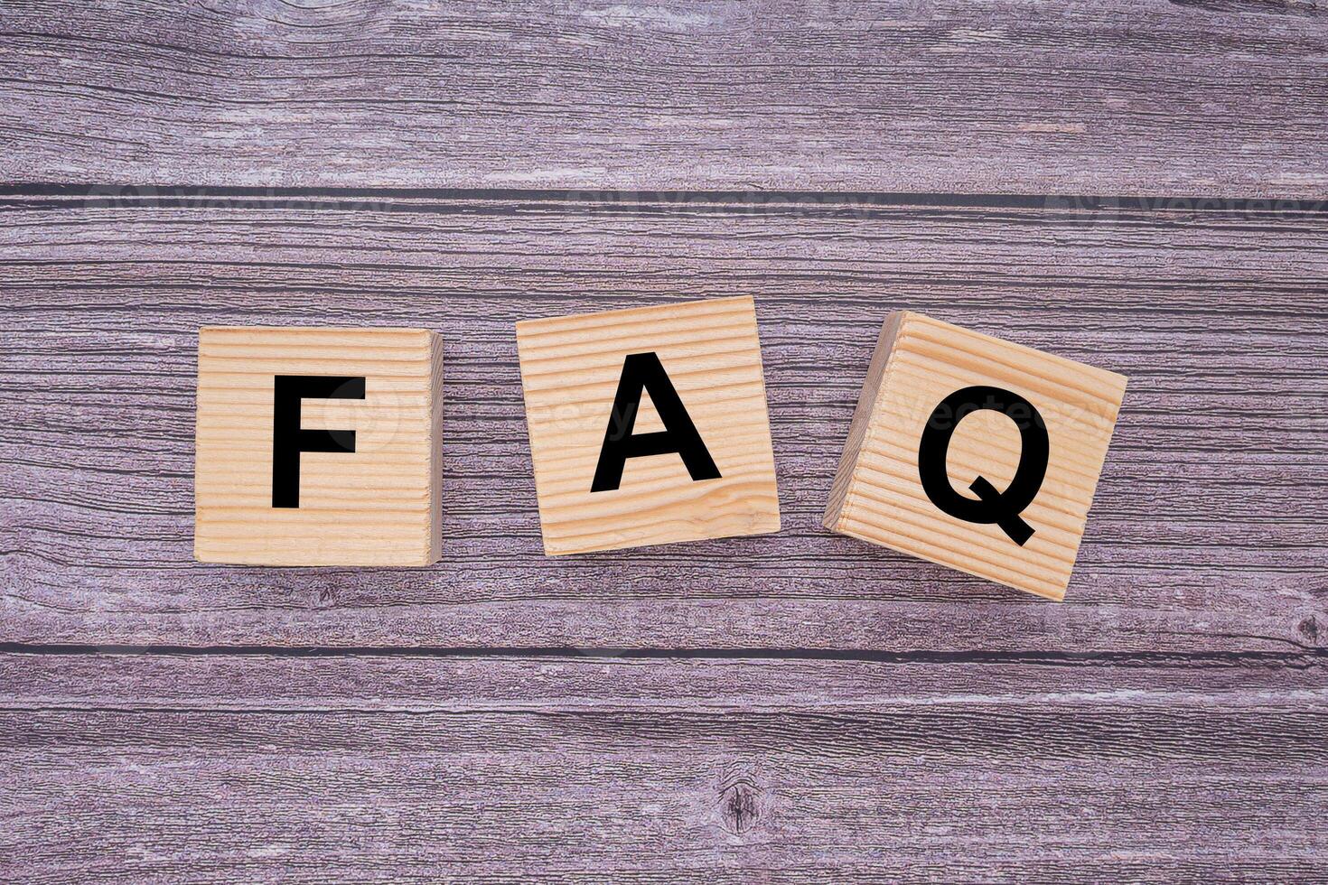 The FAQ word is written on wooden cubes on wooden table background. Frequently asked questions. Top view. Close-up photo