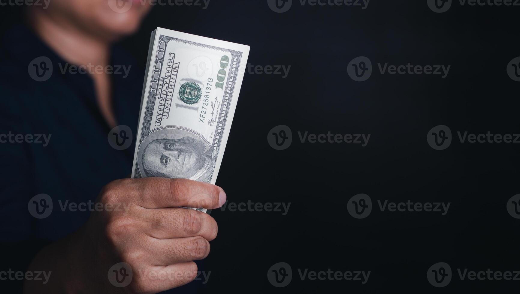 Hand holding of a US dollars banknote with a black background while standing in the studio. Close-up photo. Space for text photo