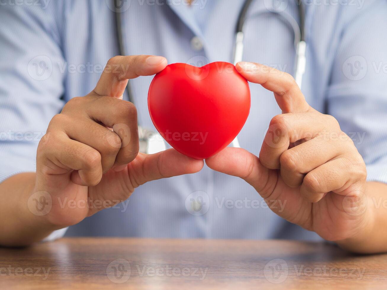 Hand of a doctor showing a red heart shape while sitting in the hospital or clinic. Close-up photo. Space for text. Medical and encouragement concep photo