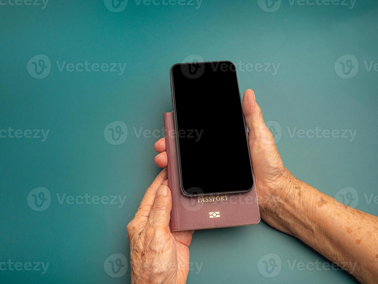 Hands of a senior woman holding a passport and smartphone on a green background. Space for text. Close-up photo. Aged people, communication and travel concept photo