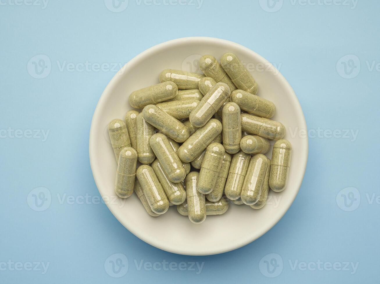Close-up of Andrographis paniculata capsules are in a dish isolated on blue background. Space for text. Herbal, medicine, and healthcare concept photo