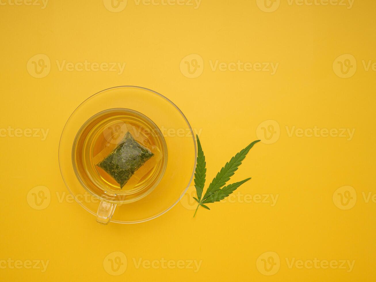 The top view of hemp tea in a teacup and marijuana leaves isolated on a yellow background. Cannabis herbal tea. Flat lay. Selective focus with copy space for text. Relaxation concept photo