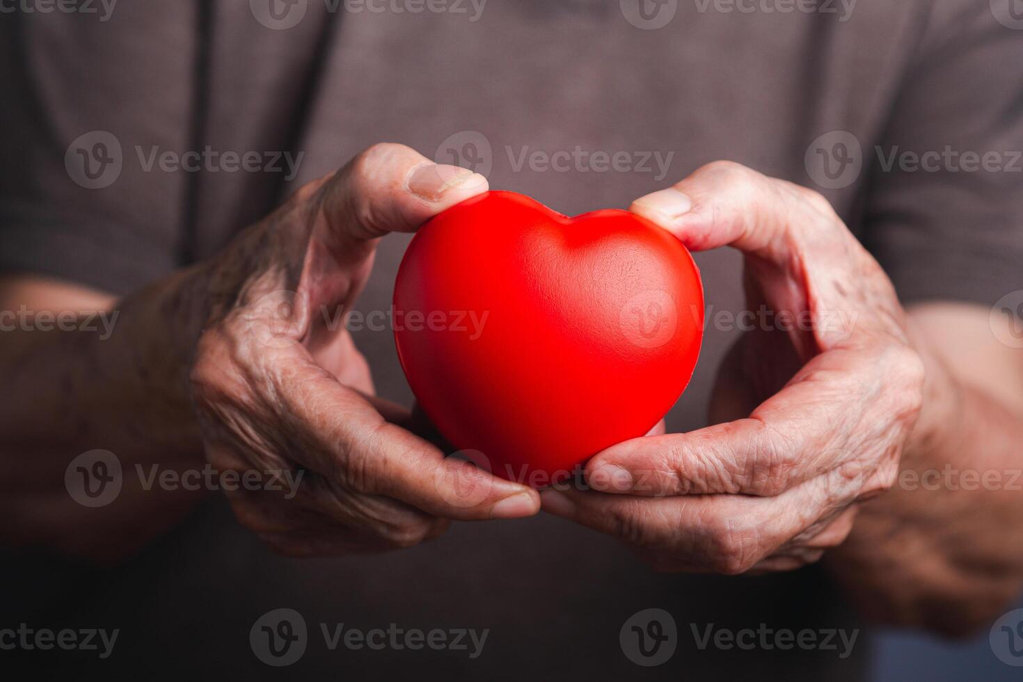 Hand of a senior woman holding a red heart shape. Close-up photo. Aged people and healthcare concept photo