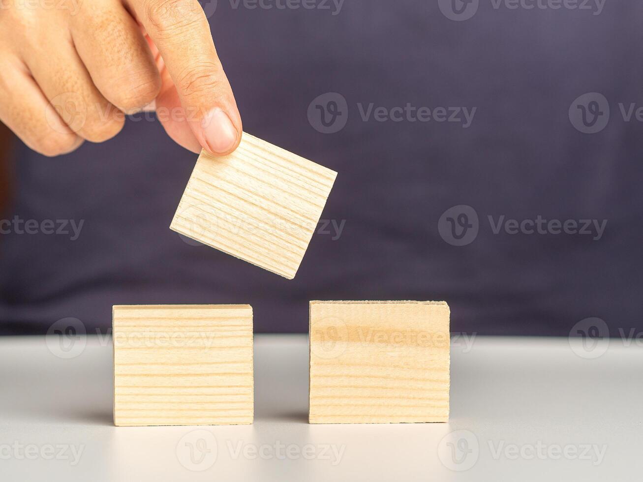 Close-up of hand holding empty wooden block on white table. Space for text photo