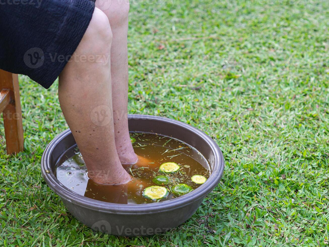 Close-up of the foot spa with herbs water for relaxation treatment. A senior woman who has ankle pain uses herbal treatment to relax the muscles by soaking warm water that is boiled from herbs photo