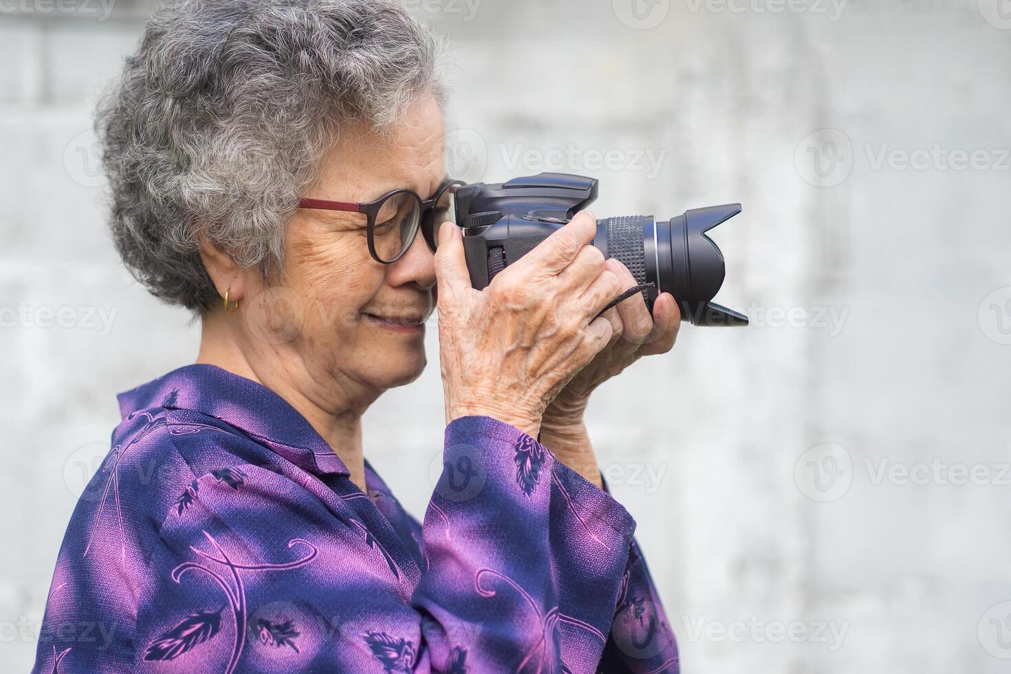 Happy senior woman taking photographs with a digital camera while standing outdoors. Aged people photographer and relaxation concept photo