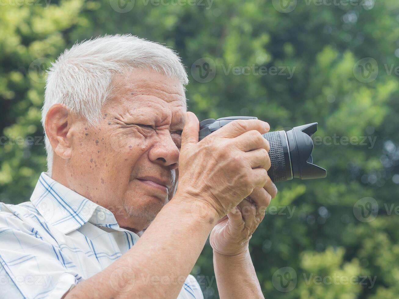 Happy senior man taking photographs with a digital camera while standing outdoors. Aged people photographer and relaxation concept photo