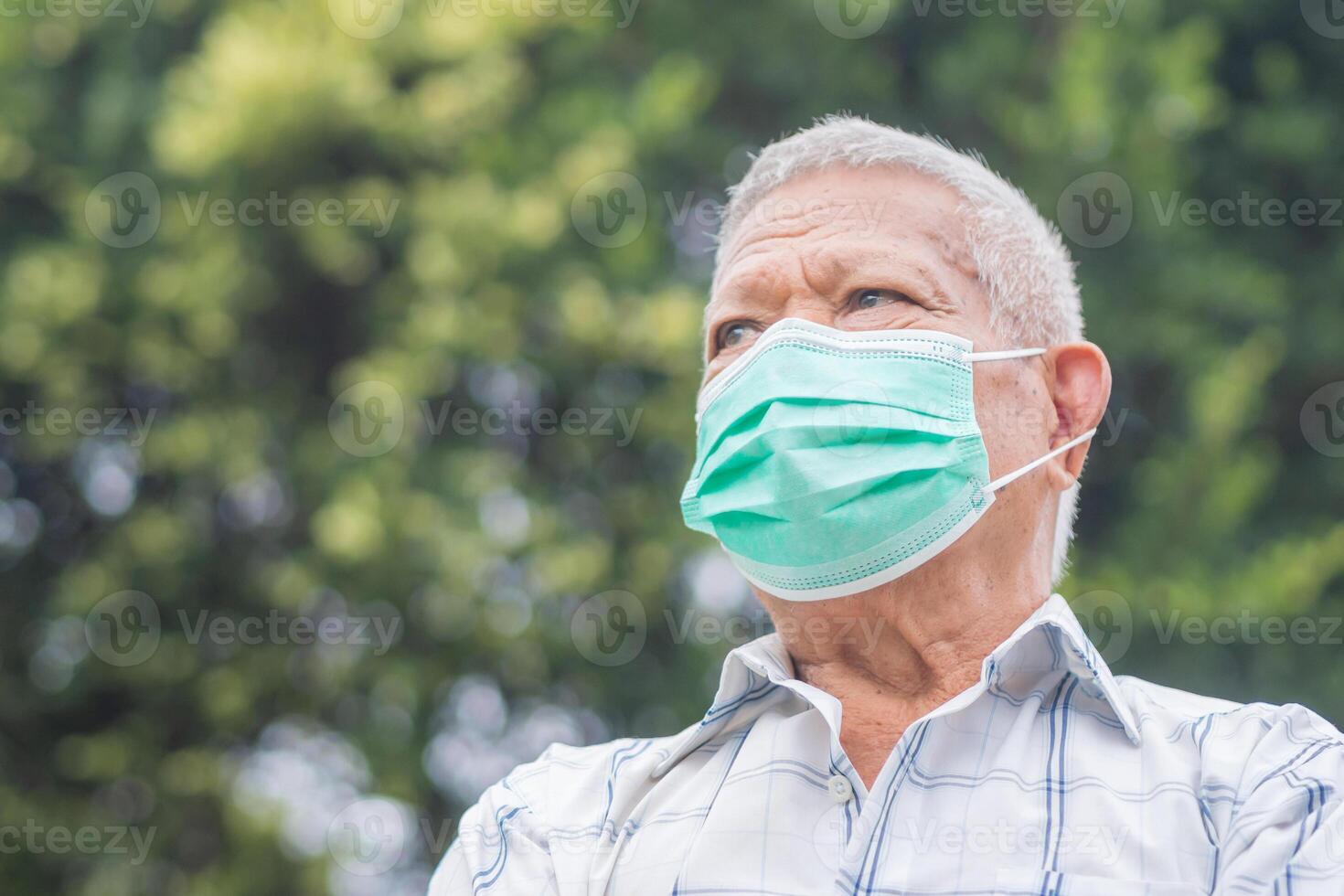 Portrait of a senior man with short gray hair, wearing a face mask and looking up while standing outdoor. Space for text. Aged people and healthcare concept photo