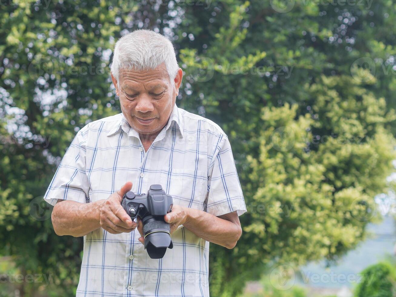 Portrait of a senior man holding and looking at a digital camera for preparing to take photography while standing outdoors. Aged people photographer and relaxation concept photo