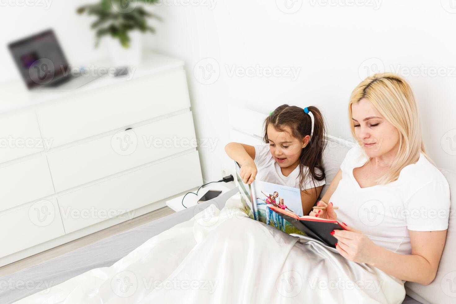 Cute little girl and her mother lying on a bed photo