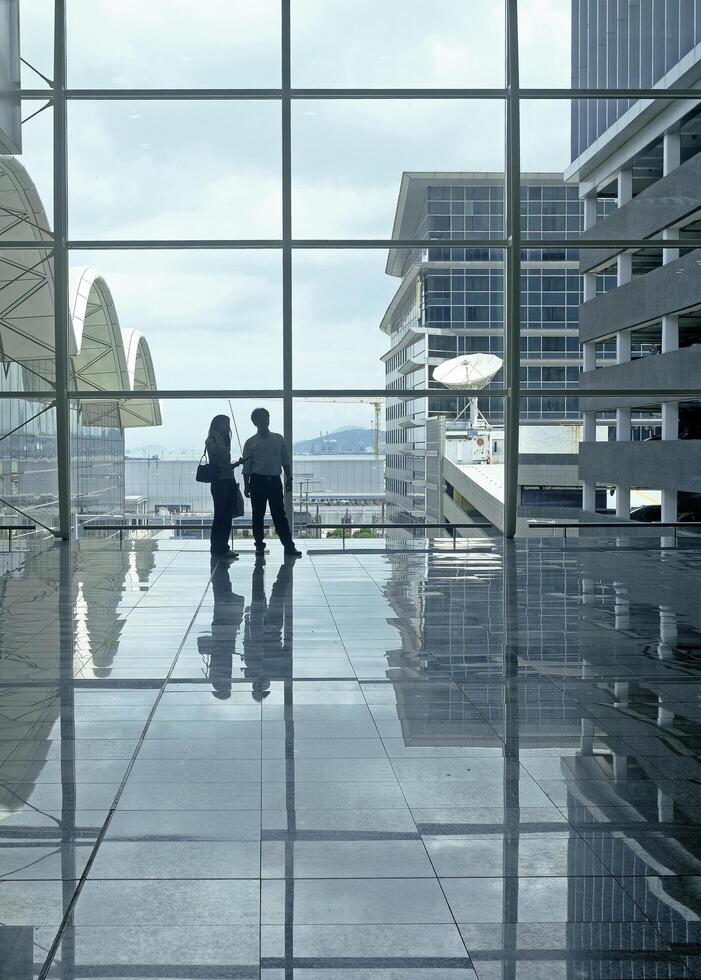 Airport terminal huge glass window with view of departure buildings and silhouette of two persons photo